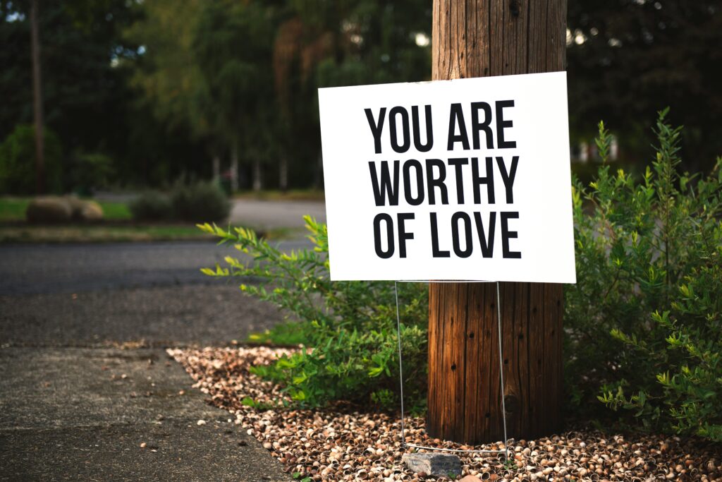 A sign next to a tree that says "You Are Worthy Of Love" a gentle reminder of self-worth, healing, and emotional self-care.