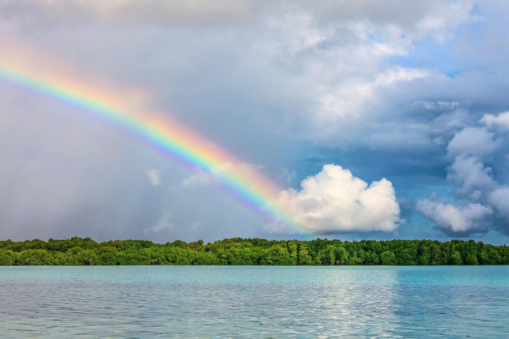 Lush green landscape with blue water and a rainbow, symbolizing calm, renewal, and ways to boost your energy naturally.