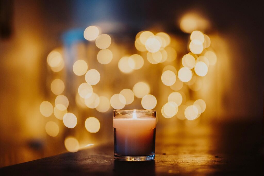 Lit soy candle with golden flame in cozy home setting, blurred background of glowing candles, creating warm ambiance for mindfulness, meditation, self-care, relaxation, and stress relief