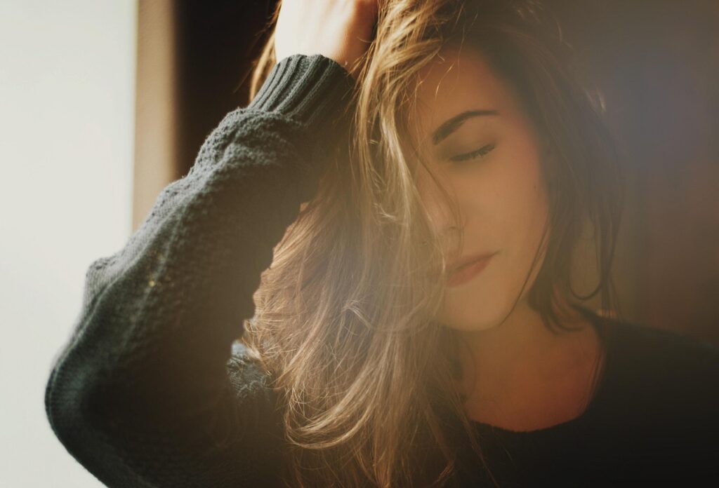 Woman standing in morning light covering her face, showing struggle with mornings, symbolizing morning rituals