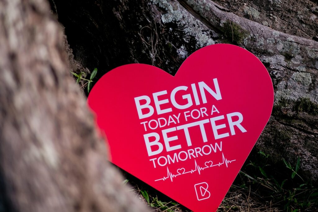 Red heart-shaped card with the words “Start today for a better tomorrow” resting against a tree trunk in a natural outdoor setting, symbolizing self-love, personal growth, and wellness transformation.